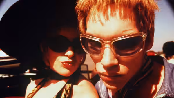 Couple in sunglasses lean close together outdoors near a vehicle