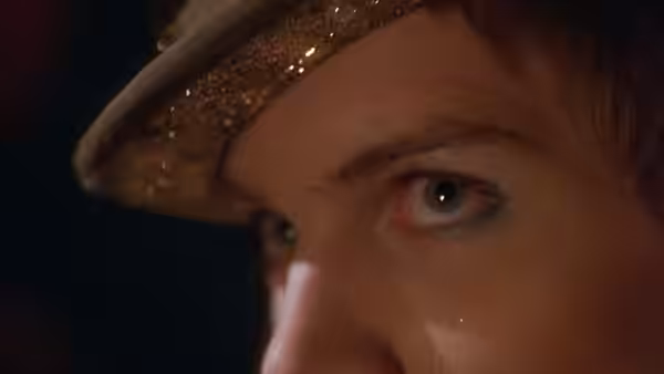 Close-up of eye with glitter makeup beneath sequined hat brim