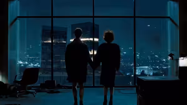 Two people holding hands in front of a city skyline at night