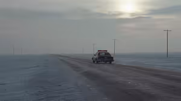A police car driving down an empty snowy highway at dusk