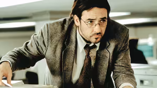 Craig (John Cusack) leaning over a desk in an office