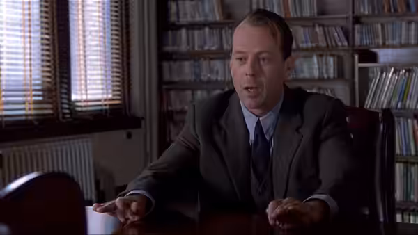 Malcolm Crowe (Bruce Willis) seated at desk in office with bookshelves behind him