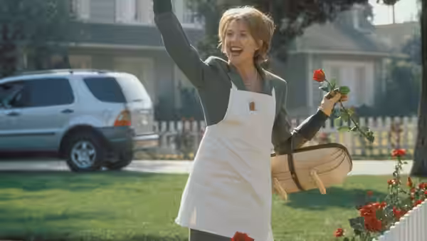 Carolyn Burnham (Annette Bening) waving while holding roses on a suburban lawn