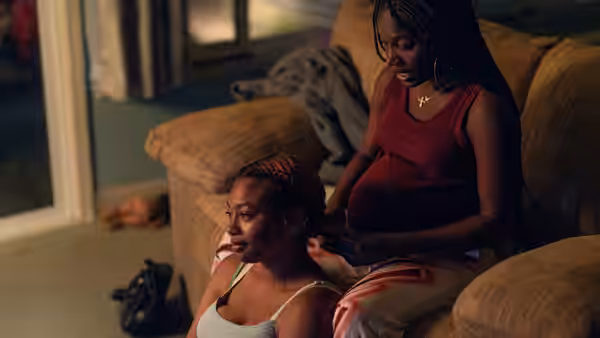 A pregnant woman in red sits on a couch beside a younger woman