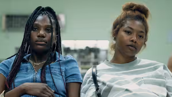 Gia (Tia Nomore) stands beside a braided woman in a community office
