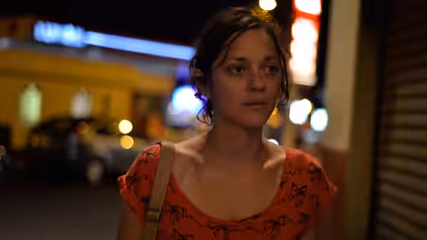Sandra (Marion Cotillard) stands on a neon-lit street at night wearing orange