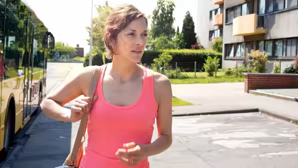 Sandra (Marion Cotillard) walks briskly beside a yellow bus on a sunny street