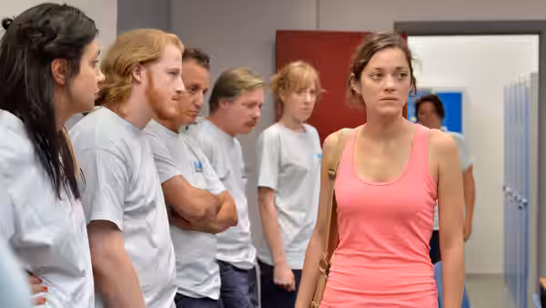 Sandra (Marion Cotillard) walks through a corridor ahead of coworkers in white shirts