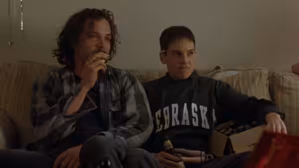 John Lotter (Peter Sarsgaard) drinking from a bottle beside Brandon (Hilary Swank) on a couch