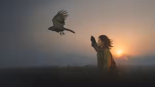 Helen (Claire Foy) raising her arm as a hawk flies overhead at sunset