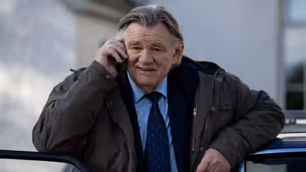 Dad (Brendan Gleeson) talking on a phone while leaning on a car