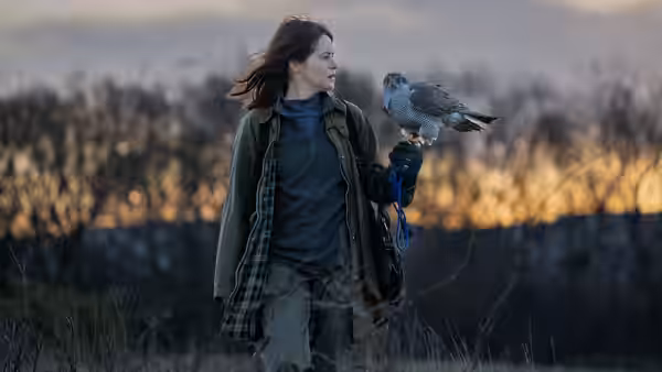 Helen (Claire Foy) with a hawk perched on her gloved hand in a field