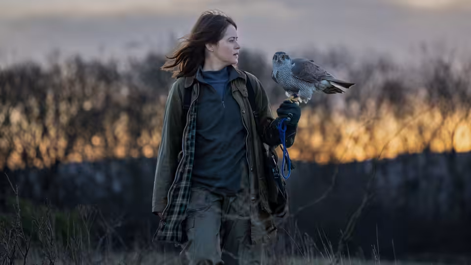 Helen (Claire Foy) with a hawk perched on her gloved hand in a field