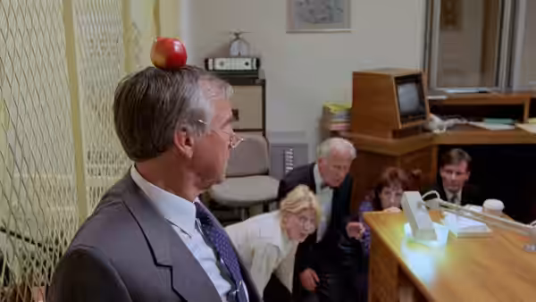 Judge (Geoffrey Palmer) with an apple balanced on his head in an office