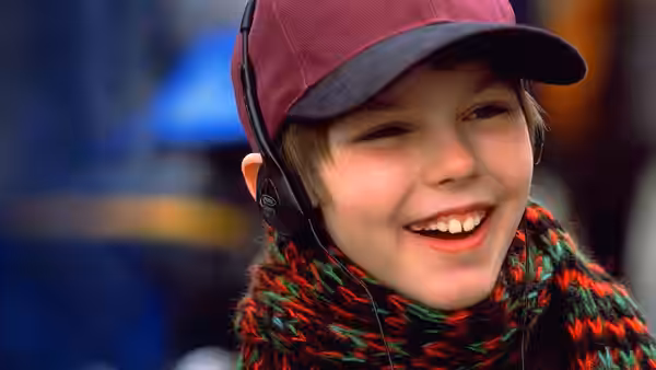 Marcus Brewer (Nicholas Hoult) smiles wearing headphones and a red cap
