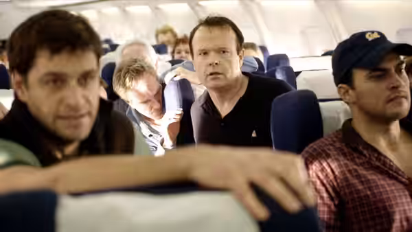 Several passengers sit tensely in airplane seats looking forward