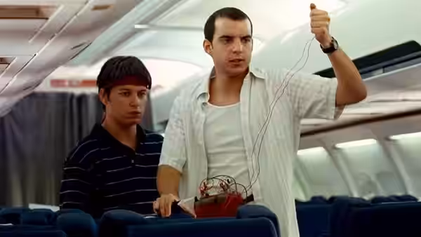 Two men stand in an airplane cabin holding a device with wires