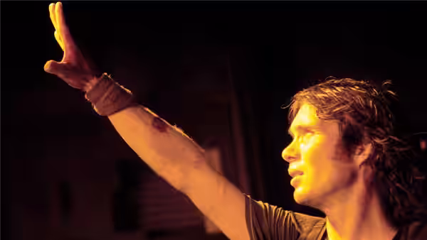 Capa (Cillian Murphy) raising his bandaged arm in dim light