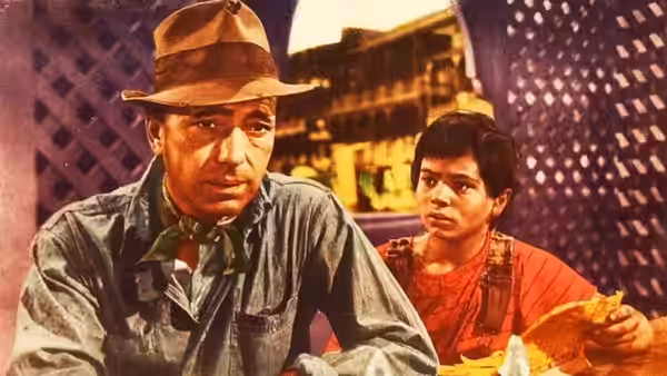 Fred C. Dobbs (Humphrey Bogart) sitting beside a boy in a marketplace at night