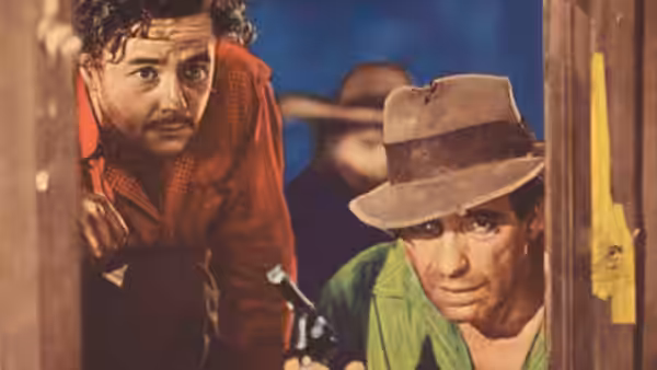 Fred C. Dobbs (Humphrey Bogart) holding a gun while peering through a doorway with another man