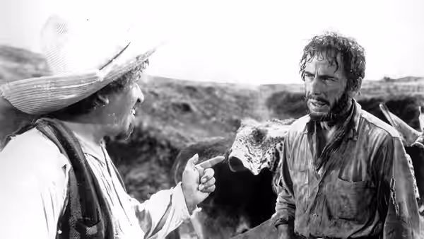 Bob Curtin (Tim Holt) pointing at Fred C. Dobbs (Humphrey Bogart) in a barren landscape