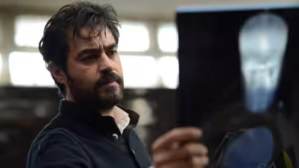 A bearded man examines an X-ray film in a bright room