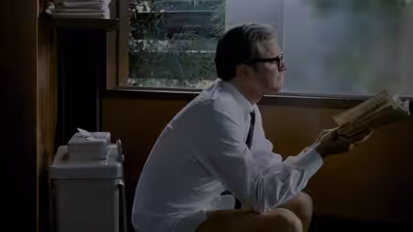 George (Colin Firth) sits beside a window, reading a book