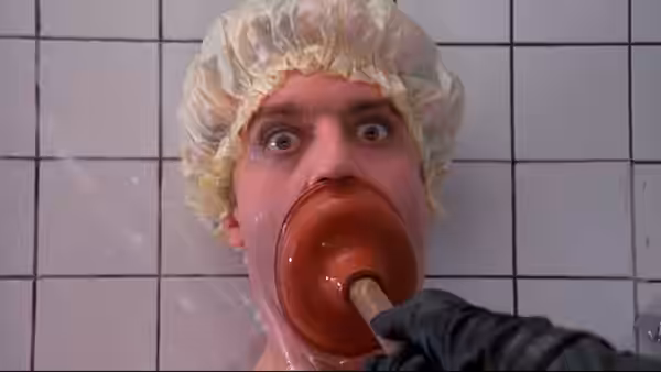 Man in shower cap with plunger in mouth in tiled bathroom