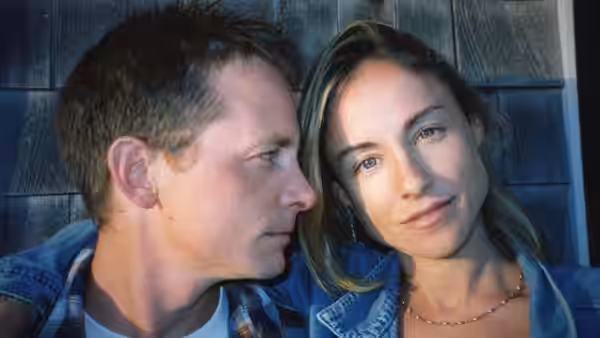 Michael J. Fox and Tracy Pollan sit close together against a wooden wall