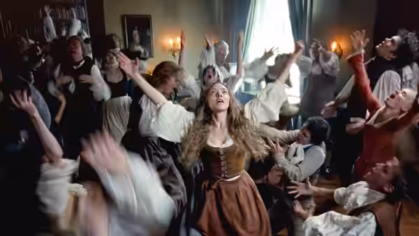 Ann Lee (Amanda Seyfried) raising her arms amid a group of worshippers indoors