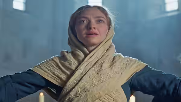 Ann Lee (Amanda Seyfried) with arms outstretched in a dimly lit room