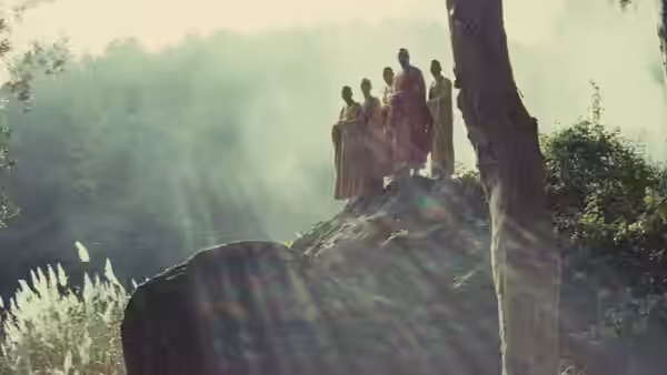 Four robed figures stand atop a rocky outcrop in the mist