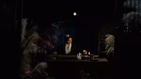 A woman sits behind a desk in a dark room