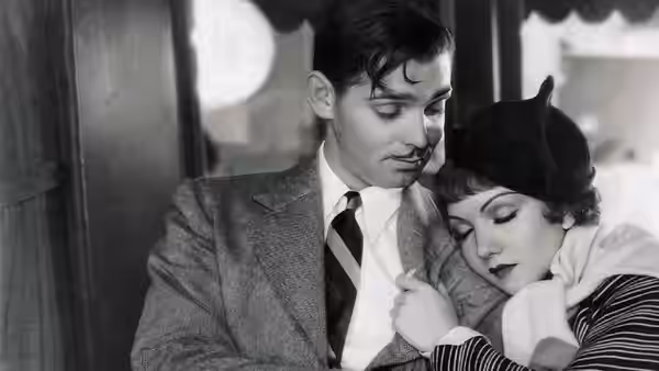 Peter Warne (Clark Gable) and Ellie Andrews (Claudette Colbert) embrace closely by a window