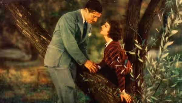 Peter Warne (Clark Gable) leans toward Ellie Andrews (Claudette Colbert) against a tree