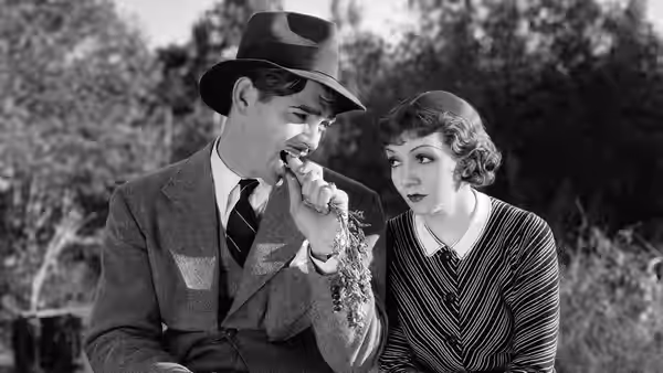 Peter Warne (Clark Gable) eats from a bunch as Ellie Andrews (Claudette Colbert) watches