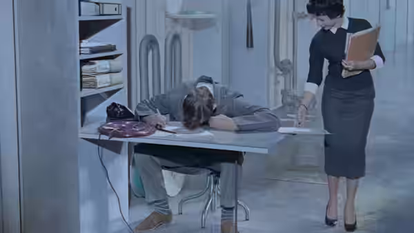 Monsieur Hulot sleeps at a desk as the housekeeper stands beside him
