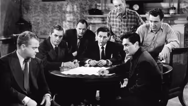 A group of suited men gather around papers on a table