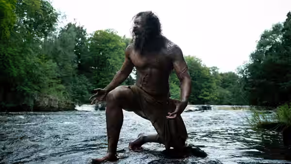 Samson (Chi Lewis-Parry) kneeling in a river with trees in the background