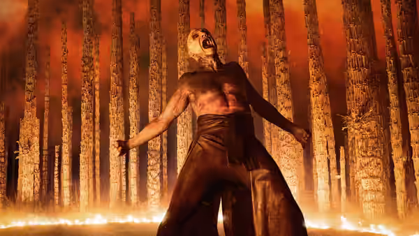 Samson (Chi Lewis-Parry) standing with arms spread in a burning forest