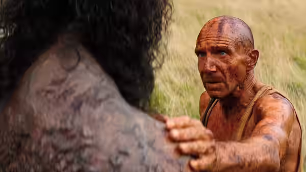 a bald man resting his hand on the shoulder of a tattooed man in a field