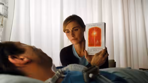 A woman showing a book to Jean-Dominique Bauby (Mathieu Amalric) lying in a hospital bed