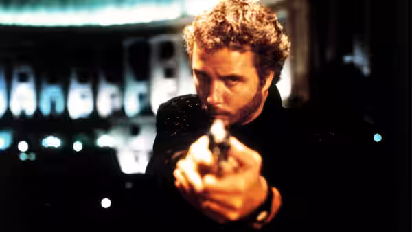 Will Graham (William Petersen) aiming a handgun forward in a dark room with blurred lights