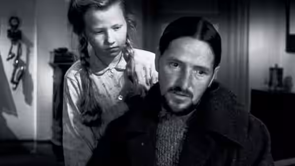Young girl with braids standing behind a bearded man in a room