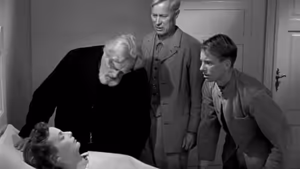 Several men leaning over a woman lying in bed inside a room