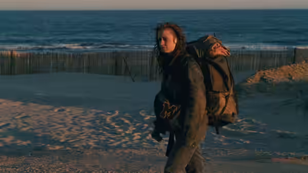 Mona (Sandrine Bonnaire) crosses a beach at dusk wearing a backpack