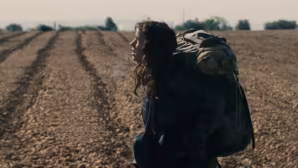 Mona (Sandrine Bonnaire) stands in a plowed field with a heavy backpack