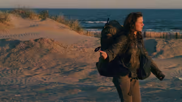 Mona (Sandrine Bonnaire) walks along a sandy beach carrying a large backpack