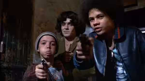 Three youths point handguns toward the camera in a derelict room
