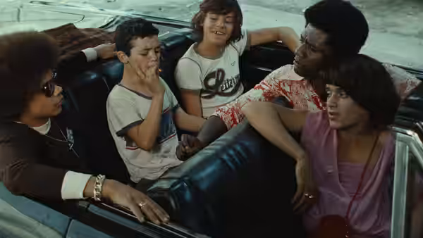 Five young people sit together inside a convertible car on the street